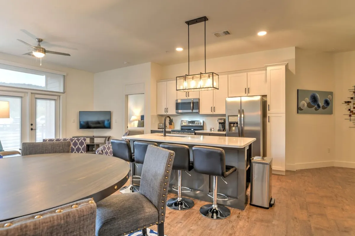 View of a modern kitchen island and dining table, with sleek appliances and vibrant wall art. The kitchen and dining space are visually linked, creating a welcoming area for shared meals or morning coffee.