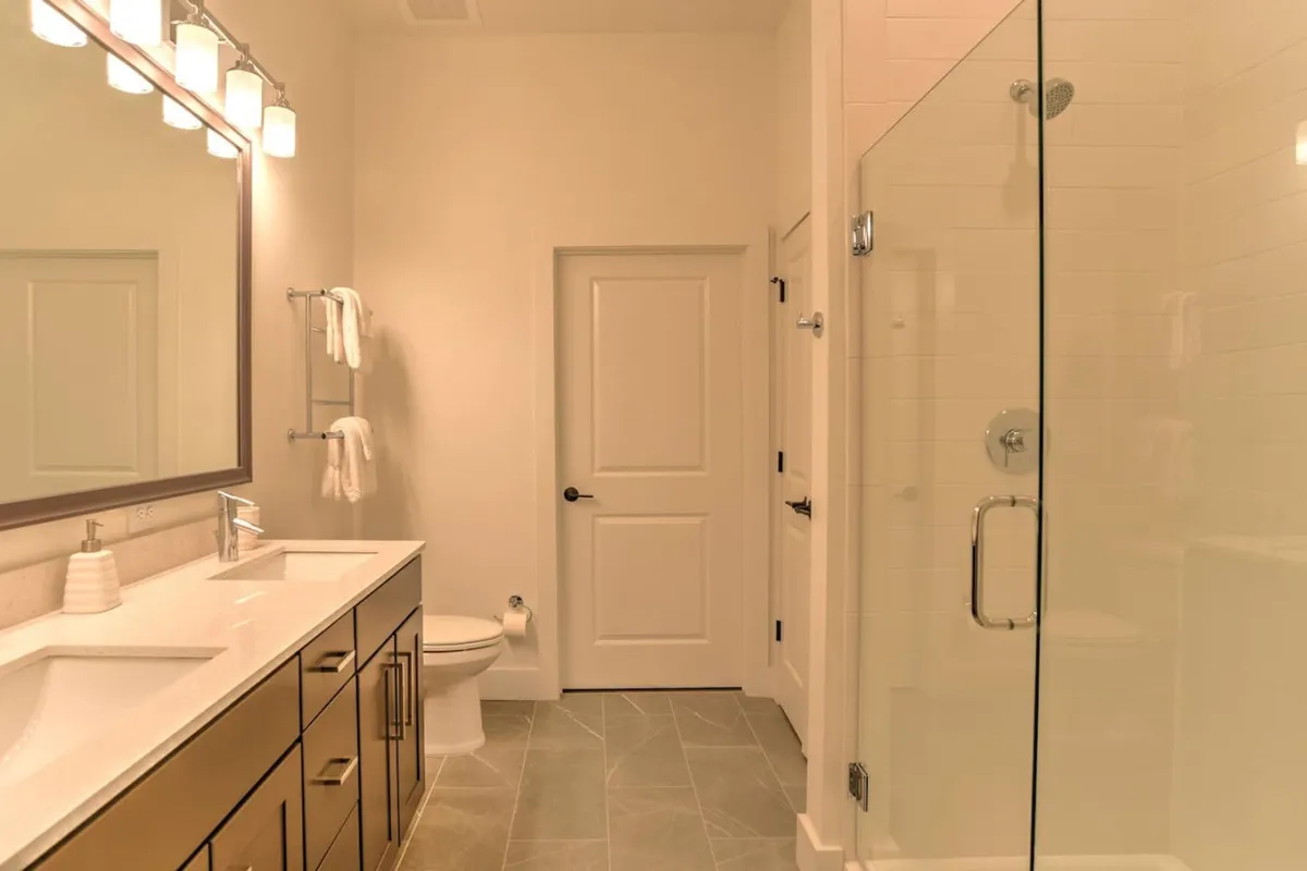 A stylish, modern bathroom with a spacious glass shower, wide vanity with sink, large mirror, and contemporary fixtures. The clean lines and soothing palette create a spa-like ambiance ideal for refreshing after a long day.