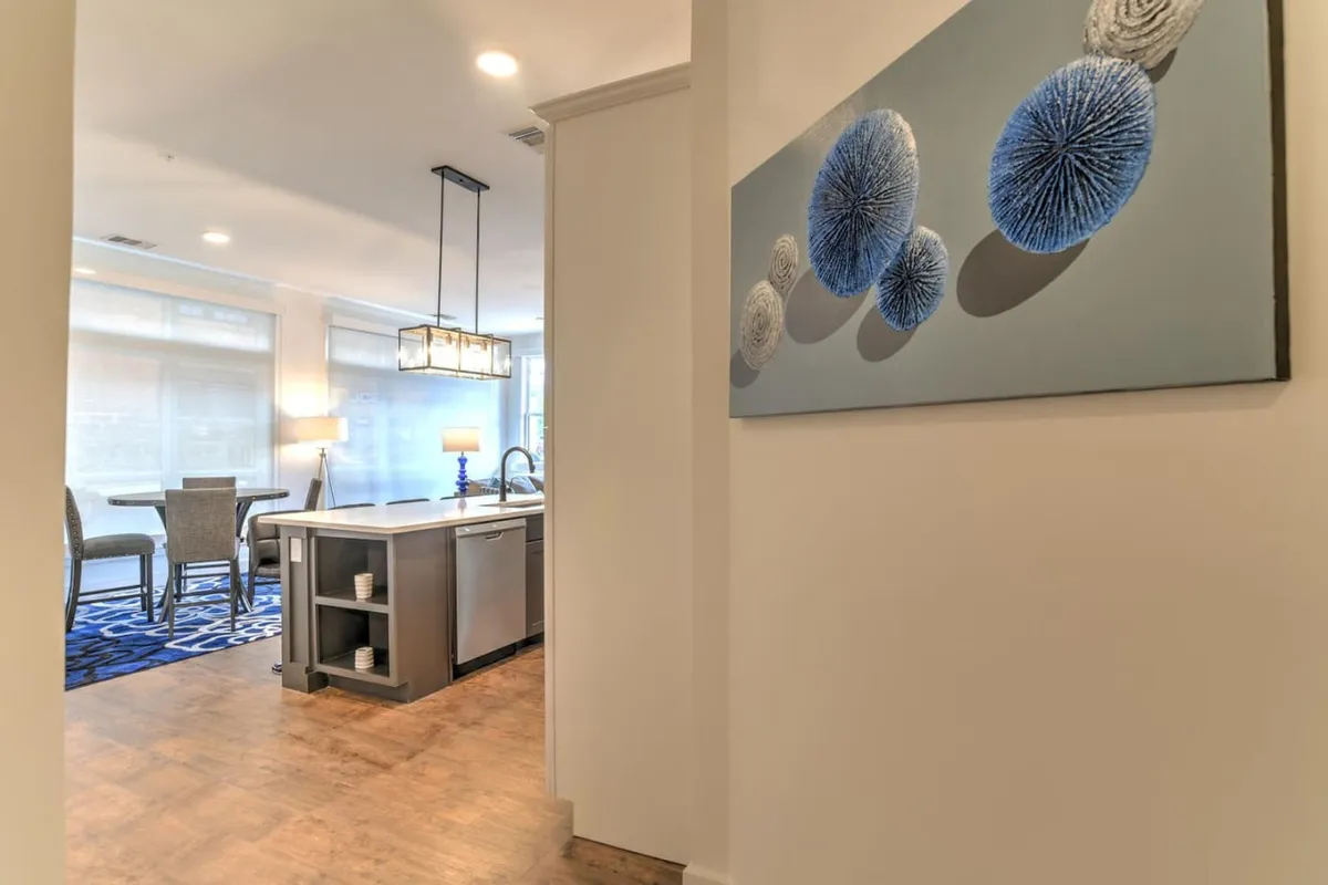 A contemporary kitchen island is the focal point, complemented by stylish blue artwork and a spacious dining area set just beyond. The open-plan design encourages both culinary creativity and relaxed gatherings, capturing the vibrant social energy of the home’s heart.